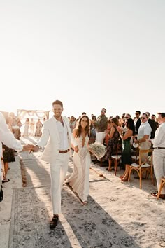 a man and woman are walking down the aisle at an outdoor wedding in white suits