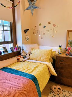 a bed room with a neatly made bed next to a dresser and window filled with toys