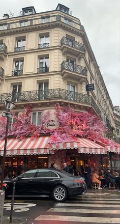 a black car parked in front of a tall building with pink flowers on it's windows