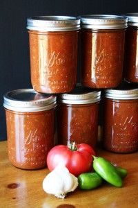 several jars filled with different kinds of food on top of a wooden table next to tomatoes and peppers