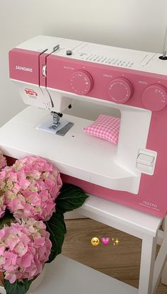 a pink and white sewing machine sitting on top of a table next to some flowers