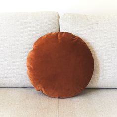 a round pillow sitting on the back of a white couch next to a brown pillow