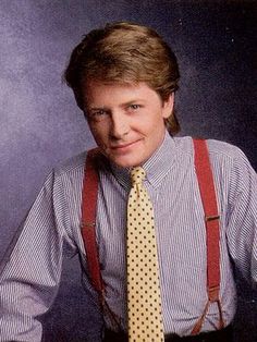 a man wearing suspenders and a tie poses for a photo in front of a purple background