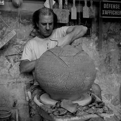 a black and white photo of a man working on a large stone vase in a shop