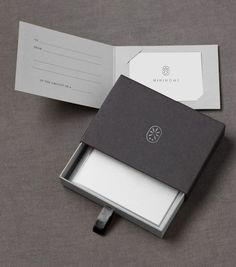 an open box with a business card in it on a gray surface next to a piece of paper