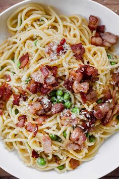 a white bowl filled with pasta and bacon on top of a wooden table next to a fork