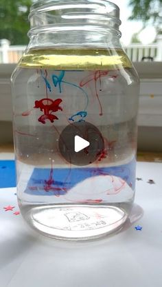 a glass jar filled with water and colored paint on top of a table next to a window