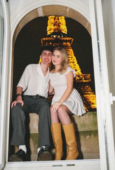 a man and woman sitting next to each other in front of the eiffel tower