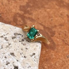 Estate/ vintage polished 10KT yellow gold ring with center, lab-created emerald + surrounding white diamonds. Timeless gold ring with a beautiful, vibrant green emerald! Size 7.25 Can be resized for an additional fee Weight: 1.8g (2) 1 pt genuine, white diamonds; SI clarity; H color Approx. 6mm x 4mm lab-created, green, rectangle center emerald Excellent estate condition Green Emerald Cut Birthstone Ring With Accent Stones, Classic Green Emerald Ring With Diamond Accents, Green Emerald Ring With Diamond Accents For Promise, Green Emerald Promise Ring With Diamond Accents, Classic Green Birthstone Ring With Diamond Accents, Emerald Cut Green Diamond Ring In 14k Gold, Fine Jewelry Rectangular Emerald Ring, Classic Rectangular Emerald Gemstone Ring, Classic Green Emerald Ring With Accent Stones