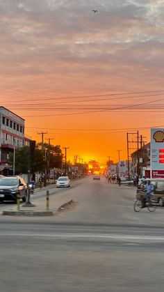 the sun is setting over a city street with cars and people riding bikes on it