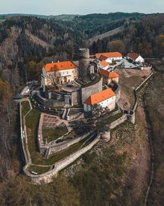 an aerial view of a castle in the middle of trees and hills with orange roofs