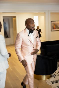 a man in a pink suit and bow tie walking through a room with other people