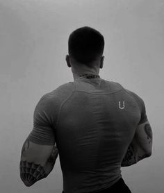 the back of a man with tattoos on his arms and shoulder, standing in front of a wall