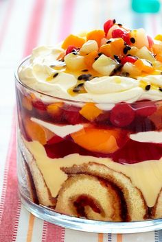 a cake with fruit toppings in a glass dish on top of a striped table cloth