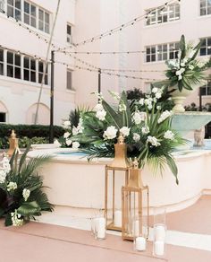 an outdoor wedding setup with candles, flowers and greenery in front of a fountain