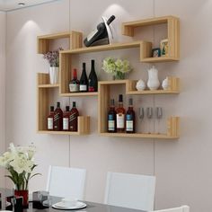 a dining room table with white chairs and shelves on the wall above it that have wine bottles, glasses, and flowers in vases