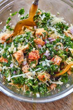 a glass bowl filled with chopped up vegetables and dressing being stirred by a wooden spoon