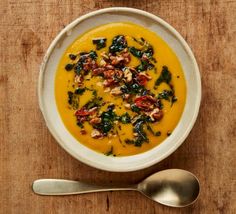 a bowl of soup with spinach and bacon in it on a wooden table next to a spoon