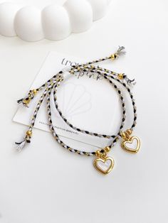 three bracelets with heart charms on white table next to card and beads, close up