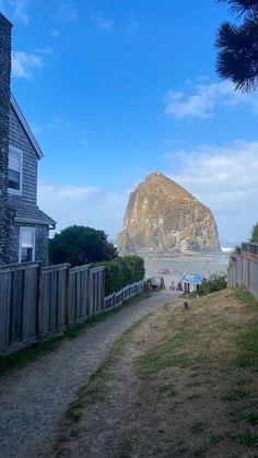 people are walking down a path to the beach near a house with a mountain in the background