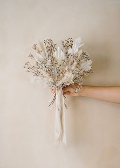 a bride's hand holding a bridal bouquet with white flowers and feathers on it