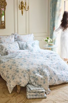 a woman standing next to a bed with blue and white bedspreads on it