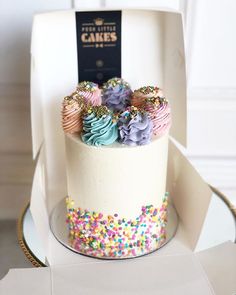 a white cake with sprinkles and frosting on top sitting in a box