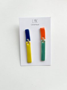 two different colored earrings on top of a piece of paper with the letter lk in it