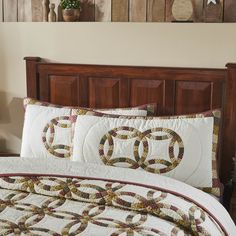 a bed with a quilt and pillows on top of it in front of a wooden headboard