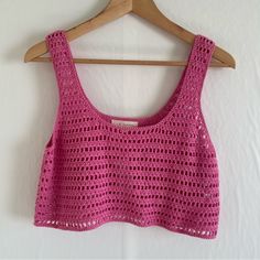 a pink crocheted top hanging on a wooden hanger next to a white wall