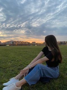 a woman sitting on the ground in a field with her legs crossed looking at the sky