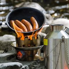 hot dogs are cooking over an open fire in a pot on the side of a river