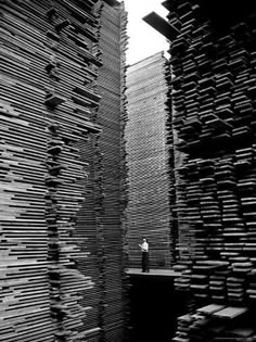 a black and white photo of a person standing in front of stacks of wooden boxes