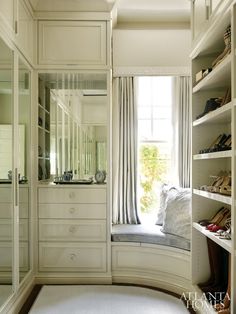 a walk in closet filled with lots of white furniture and shelves next to a window