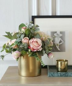 a gold vase filled with pink flowers on top of a table next to a candle