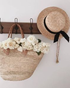 a straw bag with flowers in it hanging on a coat rack next to a hat