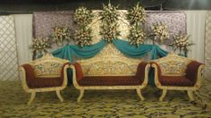 an elaborately decorated couch and two chairs in front of a wall with flowers on it