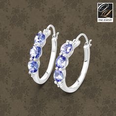 Flaunt yourself with these tanzanite & white diamond hinged hoop earrings. The natural gemstones have a combined weight of 1.99 carats and are set in .925 sterling silver with rhodium plating. The soft violet hue of these earrings adds a pop of color to any look! The understated design and vibrant stones make these earrings perfect for every occasion. Sterling Silver Three Stone Round Jewelry, Three Stone Round Earrings For Anniversary, Fine Jewelry Sterling Silver Hoop Earrings With Gemstone, Anniversary Earrings With Three Stones, Fine Jewelry Three Stone Round Earrings, Sterling Silver Hoop Earrings With Gemstones, Classic Sterling Silver Hoop Earrings With Gemstone, Sterling Silver Three-stone Earrings As A Gift, Tanzanite Birthstone Earrings As Gift