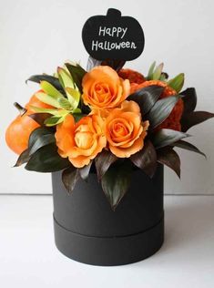 an orange flower arrangement in a black box with a happy halloween sign on it's top