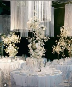 a tall vase filled with white flowers sitting on top of a table covered in chairs