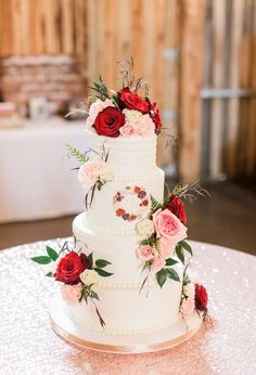 a white wedding cake with red and pink flowers on the top is sitting on a table