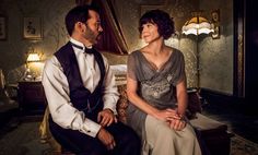 a man and woman are sitting on a couch in a room with wallpapered walls