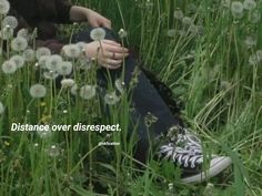 a woman sitting in the grass with her hand on top of her leg and looking at dandelions