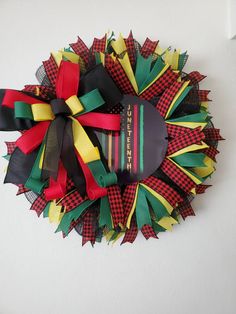 a christmas wreath made out of paper with ribbons on the top and bottom, sitting on a wall