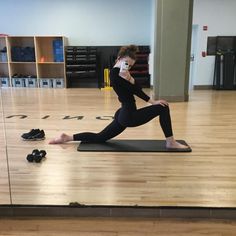 a woman in black shirt and leggings standing on yoga mat with cell phone