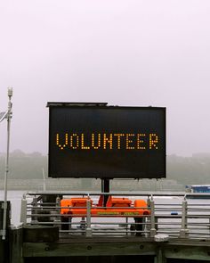 a sign that says volunteer on the side of a pier with boats in the water behind it