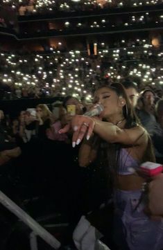 a woman standing in front of a crowd holding a cell phone to her mouth while singing into a microphone