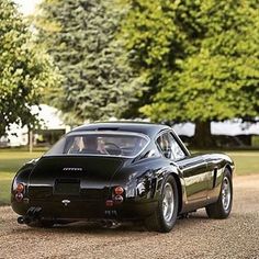 an old black sports car parked on the side of a road next to some trees