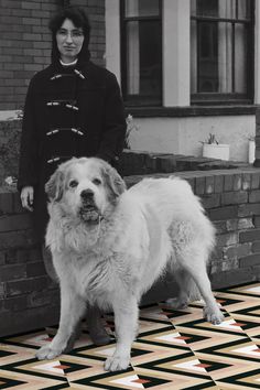 a woman standing next to a large white dog on a tiled floor in front of a brick building