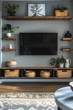 a flat screen tv mounted on a gray wall next to some baskets and potted plants